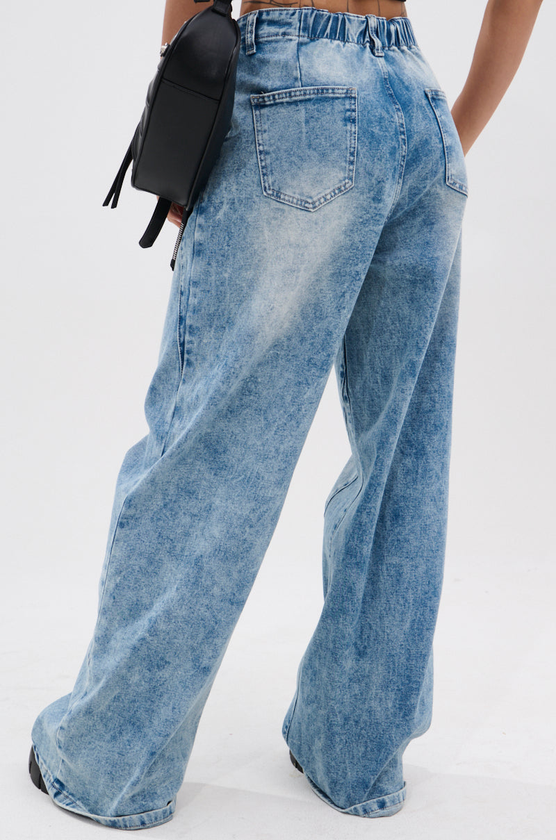 Wearing the TIED TO YOU RELAXED DENIM PANT WITH TIE BELT in a high-rise, wide-leg, light blue acid-wash style, and carrying a black shoulder bag, the person is shown from the back against a plain white background.
