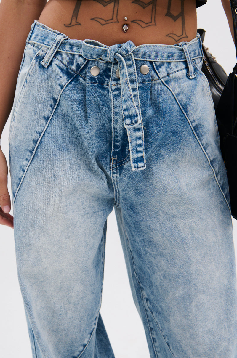 Wearing the TIED TO YOU RELAXED DENIM PANT WITH TIE BELT, a person shows off their midriff, revealing a tattoo and belly button piercing above the high-rise, light-wash jeans with matching denim tie belt.