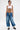 A person with short dark hair wears a white crop top and the DONT MESS WITH ME DENIM JOGGER, showing off full tattoos. They complete the streetwear look with chunky black-and-white shoes, standing against a plain white background.