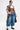 A person wears a long plaid shirt over a white crop top, showing a large "1989" tattoo, paired with DONT MESS WITH ME DENIM JOGGER jeans and chunky lace-up boots—streetwear style against a plain background.
