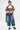 A person with short dark hair rocks a patchwork plaid long coat, white crop top, DONT MESS WITH ME DENIM JOGGER jeans with drawstring waist, chunky lace-up boots, and visible torso tattoos for a cool streetwear vibe.