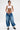 A person with short dark hair and visible tattoos rocks the DONT MESS WITH ME DENIM JOGGER—featuring big pockets and a drawstring waist—with a cropped white tank, chunky black-and-white boots, and signature streetwear flair.