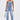 A woman wears the FEELING GRATEFUL RHINESTONE RELAXED DENIM—high-rise jeans with metallic studs and cross motifs—paired with a strapless, lace-up denim top, a silver bag, and heeled sandals.