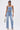 A woman wears the FEELING GRATEFUL RHINESTONE RELAXED DENIM—high-rise jeans with metallic studs and cross motifs—paired with a strapless, lace-up denim top, a silver bag, and heeled sandals.