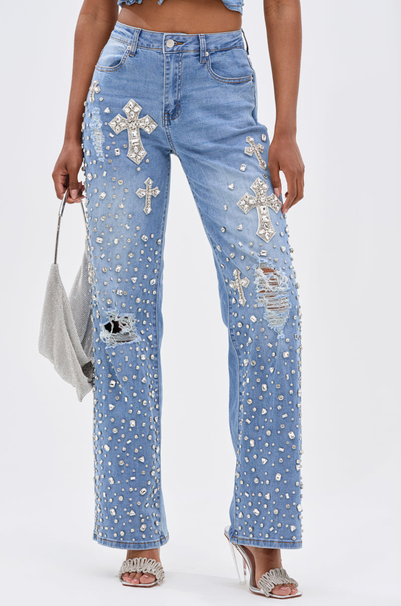Wearing FEELING GRATEFUL RHINESTONE RELAXED DENIM—high-rise relaxed jeans with silver studs, cross patches, rhinestone embellishments, and distressed details—styled with heeled sandals and a silver handbag.