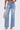 A person wearing FEELING GRATEFUL RHINESTONE RELAXED DENIM with silver cross embellishments, styled with white heels and a sparkly silver handbag.