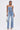 A woman in the FEELING GRATEFUL RHINESTONE RELAXED DENIM jeans, featuring rhinestones, silver studs, and cross designs, stands against a white background wearing a strapless denim crop top and holding a small silver bag.