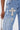 A person wears FEELING GRATEFUL RHINESTONE RELAXED DENIM, featuring rhinestones and large jeweled cross patches, holding a small silver purse. The attention is on the embellished upper leg and hip of these relaxed jeans.