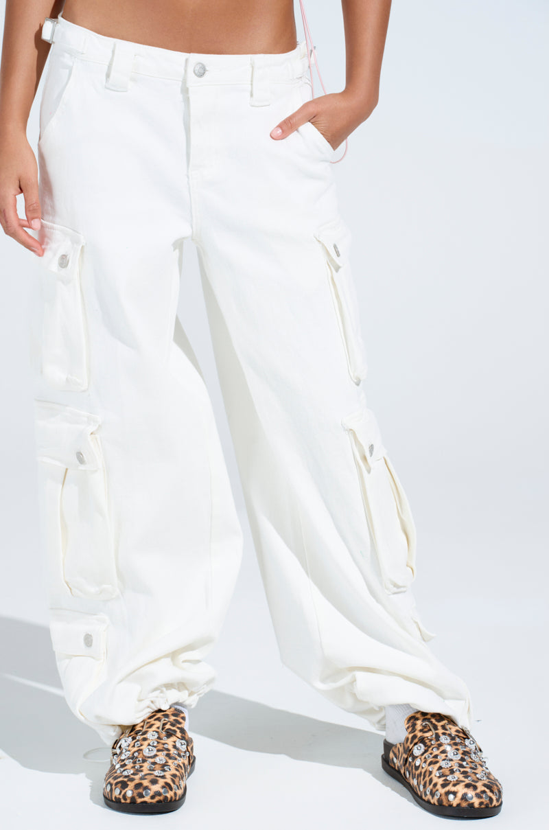 A person wearing "GET RIGHT TO IT CARGO DENIM PANT" in white-wash denim with multiple pockets and leopard print shoes stands against a plain background, casually resting their hands in the pockets.