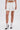 Wearing the ALWAYS GETS BETTER PLEATED MINI SKIRT, white lace-trim socks, and black heels, a person stands against a plain white background, hands by their sides and only the lower half of their body visible.