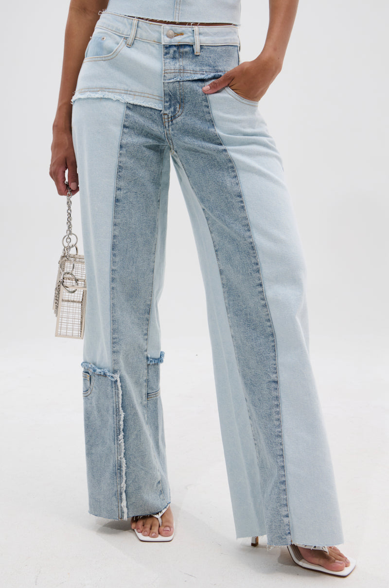 A person wearing MIX AND MATCH RELAXED DENIM PANTS—high-waisted, wide-leg jeans in two blue denim shades—with a cropped top, white heeled sandals, and a small metallic square handbag.