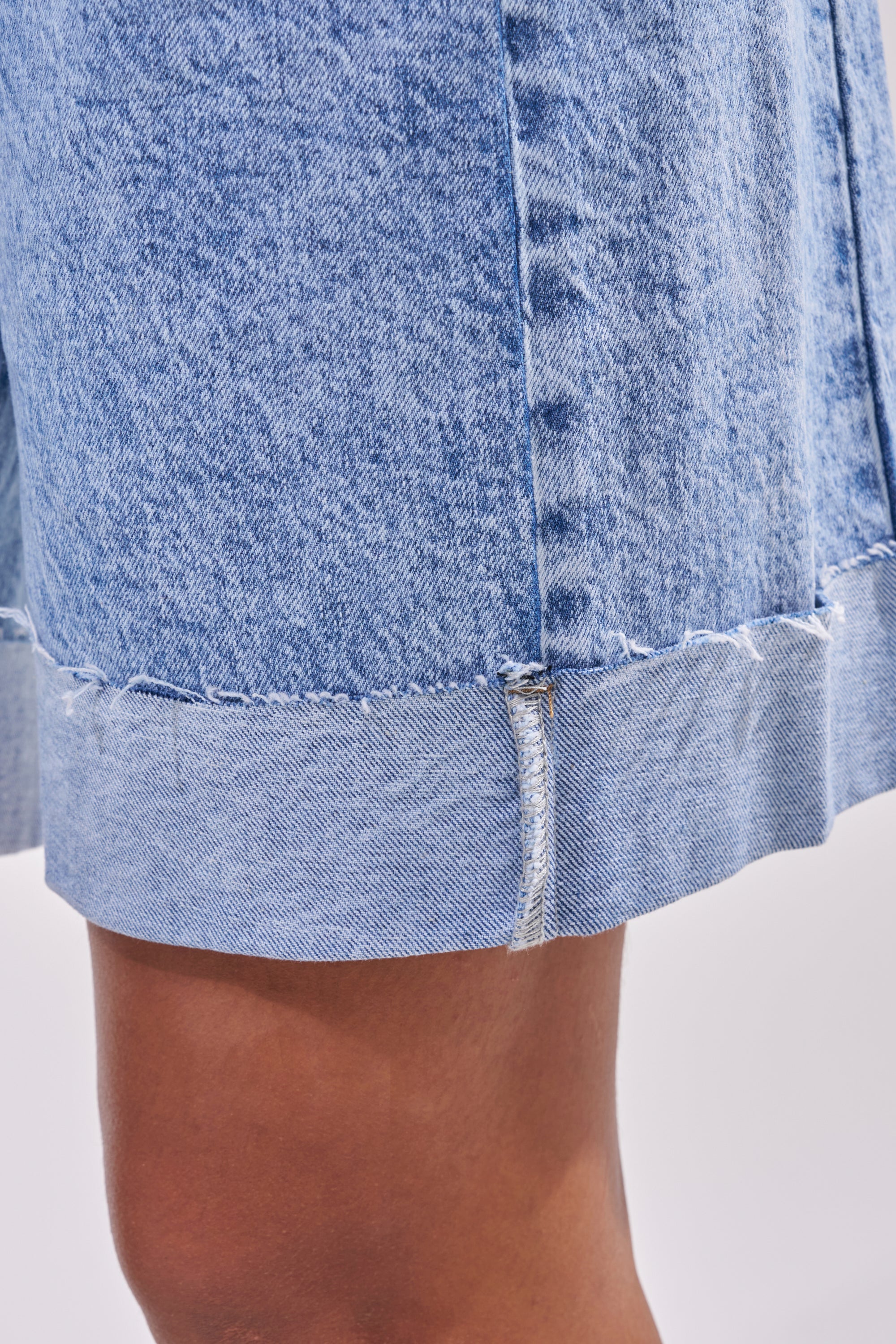 Close-up of a person's leg wearing the GONE BAD DENIM BERMUDA SHORT in light blue with a raw hem, visible stitching, and a wide-leg silhouette against a plain white background. 8
