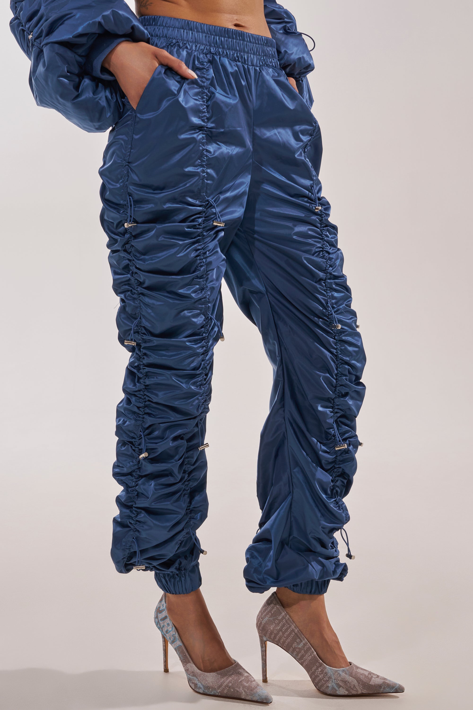 Wearing the NOT TIME FOR GAMES RUCHED JOGGER IN NAVY and light grey high heels, a person poses with one hand on their hip while their upper body is partially out of frame. 2