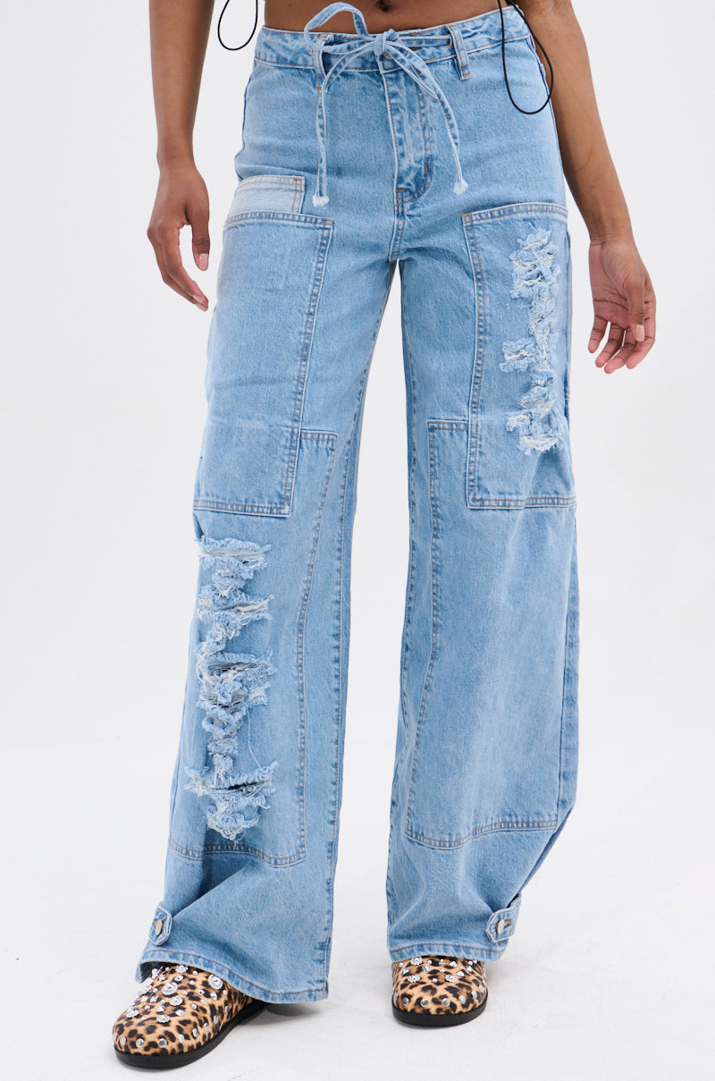 Wearing DOWN FOR WHATEVER RELAXED DENIM light blue, wide-leg ripped jeans with panel details and leopard print shoes, a person stands against a plain white background.