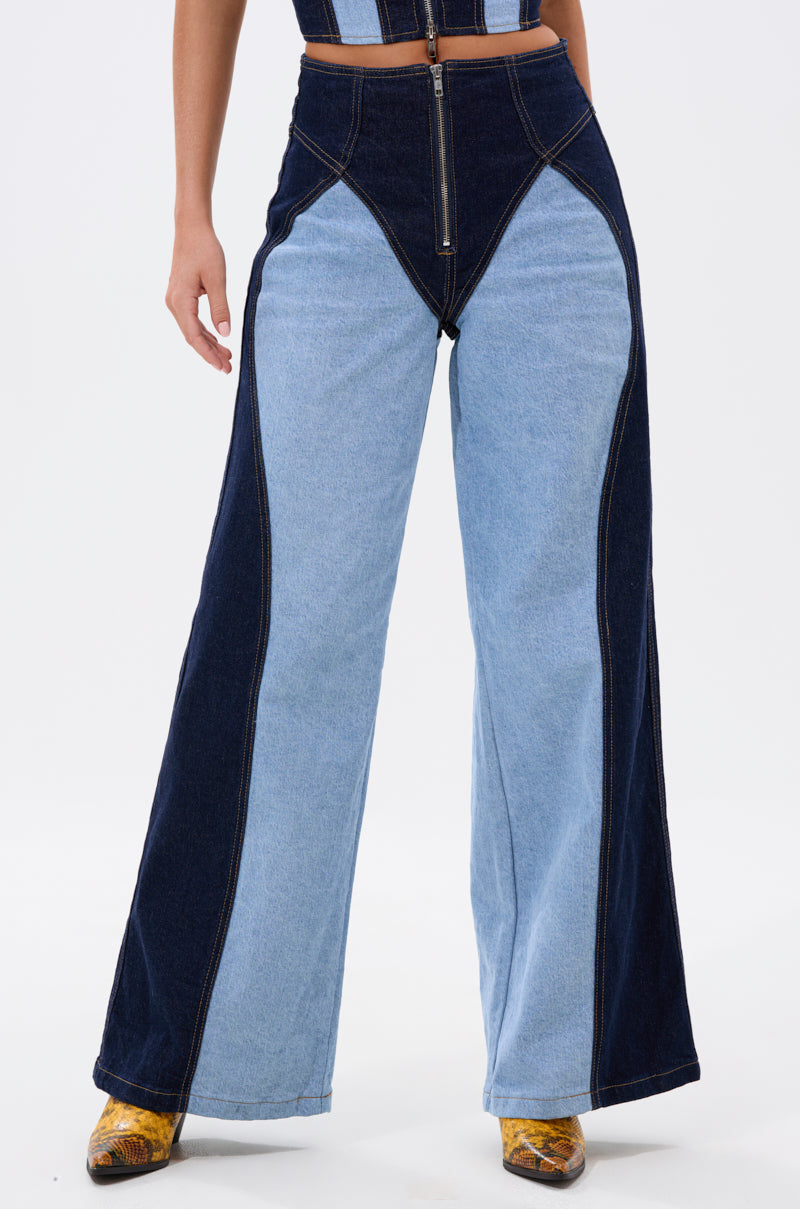 A person wears the FIRST CLASS RELAXED DENIM PANT—high-waisted, two-tone wide-leg jeans with a front zipper—and yellow patterned shoes. Their upper body is partially visible.