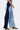 A person in profile wears the FIRST CLASS RELAXED DENIM PANT, showcasing a relaxed wide-leg fit with dark and light blue two-tone panels, styled with yellow snakeskin boots and black heels against a plain white background.