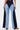 A person seen from the back wears FIRST CLASS RELAXED DENIM PANT, a high-waisted, two-tone wide-leg jean with dark and light blue panels, bold angular contrast stitching, paired with brown boots.