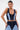A woman with slicked-back hair wears large hoop earrings and the FIRST CLASS DENIM CORSET, a contrast-paneled, zip-front crop top, styled with matching high-waisted denim pants for a modern cropped look.