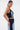 A woman with long, straight dark hair models the FIRST CLASS DENIM CORSET and matching high-waisted denim pants, posing in profile against a plain white background.