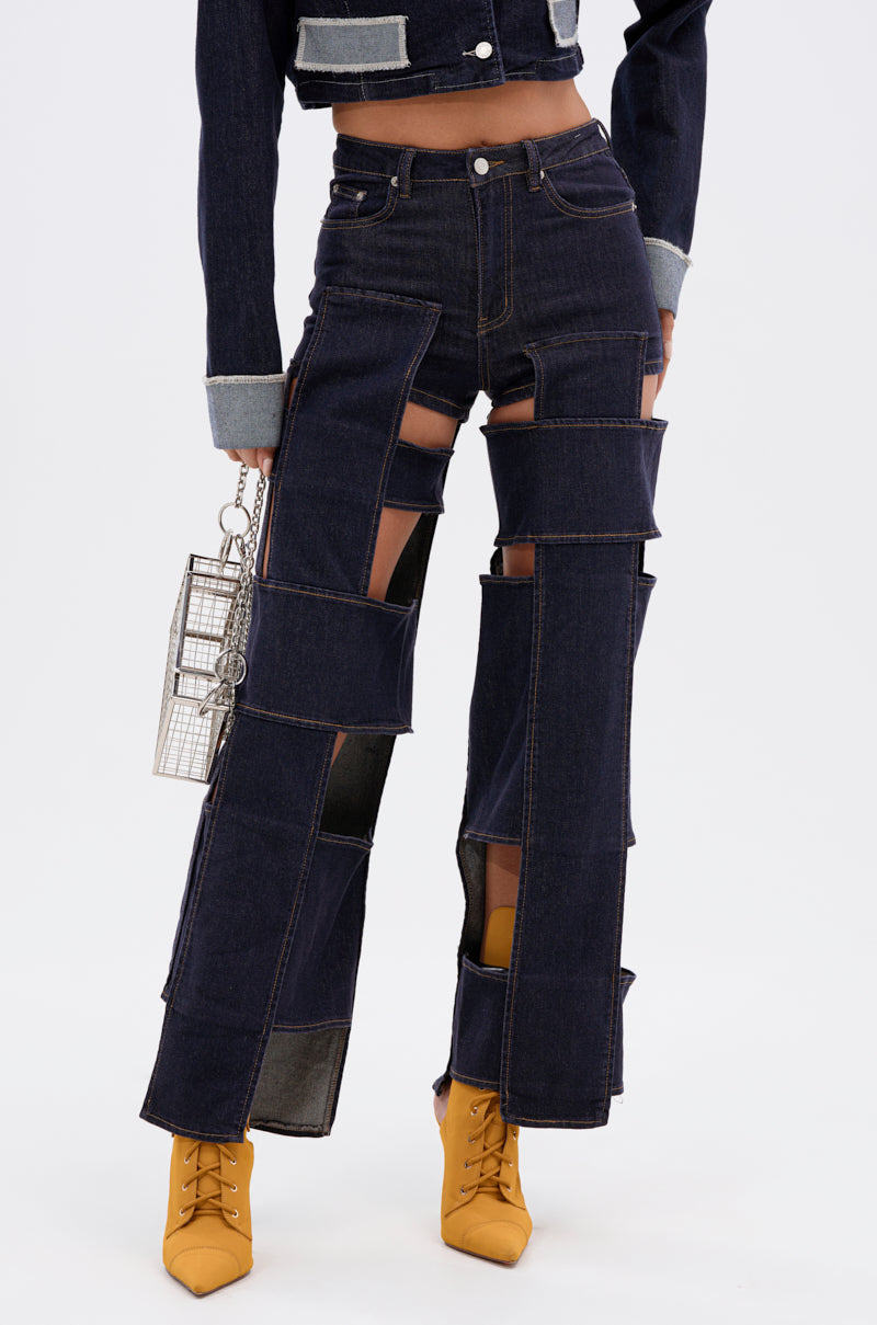A person wears the LOCKED UP FOR GOOD DENIM PANT, featuring dark wash patchwork and large cut-out panels, paired with a matching jacket, yellow pointed-toe boots, and a small metallic handbag against a plain white background.