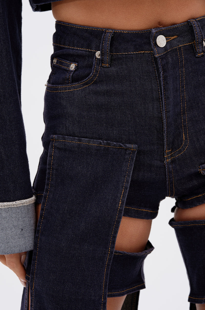 Close-up of a person wearing the LOCKED UP FOR GOOD DENIM PANT, featuring large rectangular thigh cutouts, high-rise fit, classic orange stitching, and a metal button.