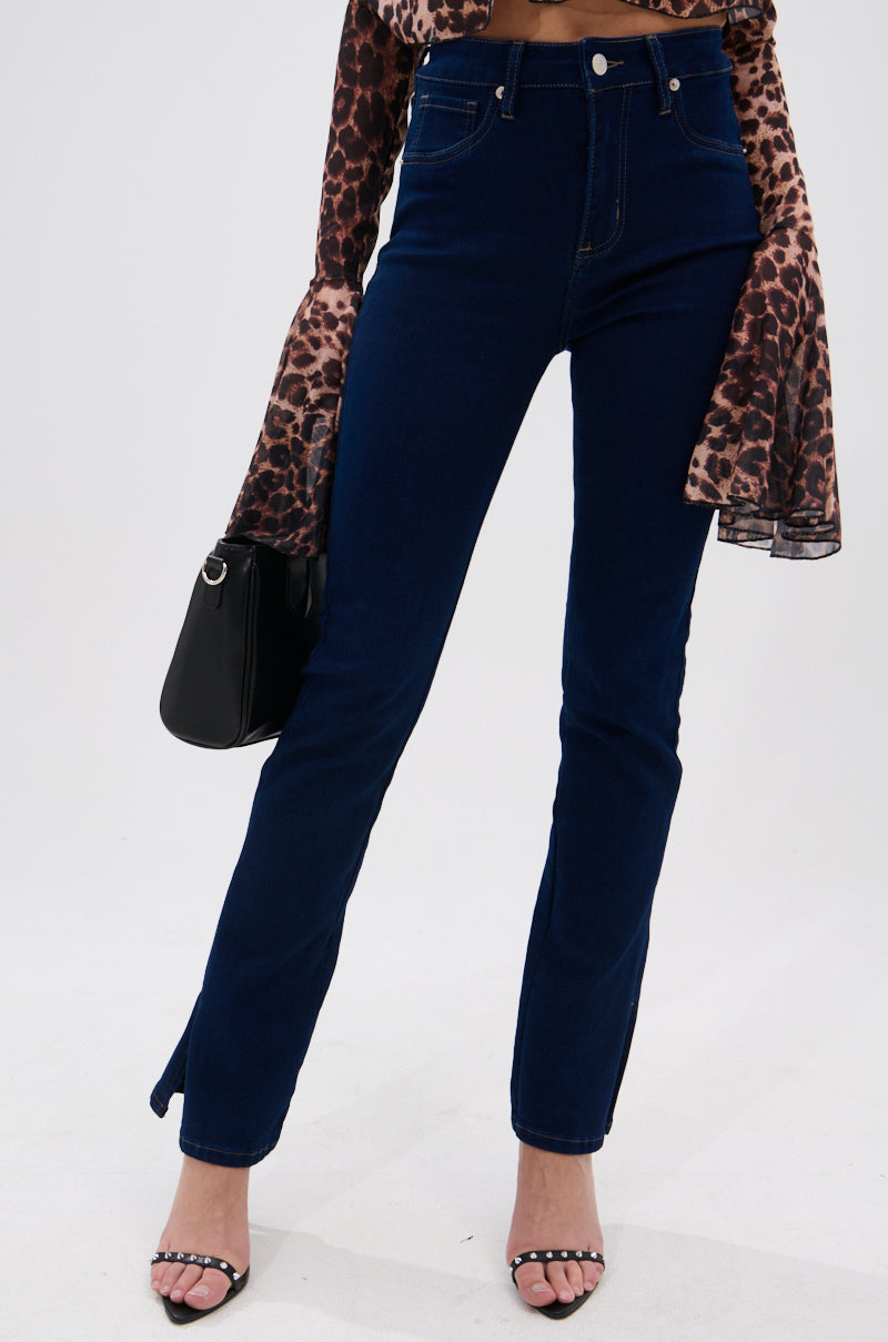A person wears THE BEST CORSET WAISTED FLARE DENIM jeans, a long-sleeve leopard print top with flared cuffs, black heeled sandals, and holds a black handbag against a plain white background.