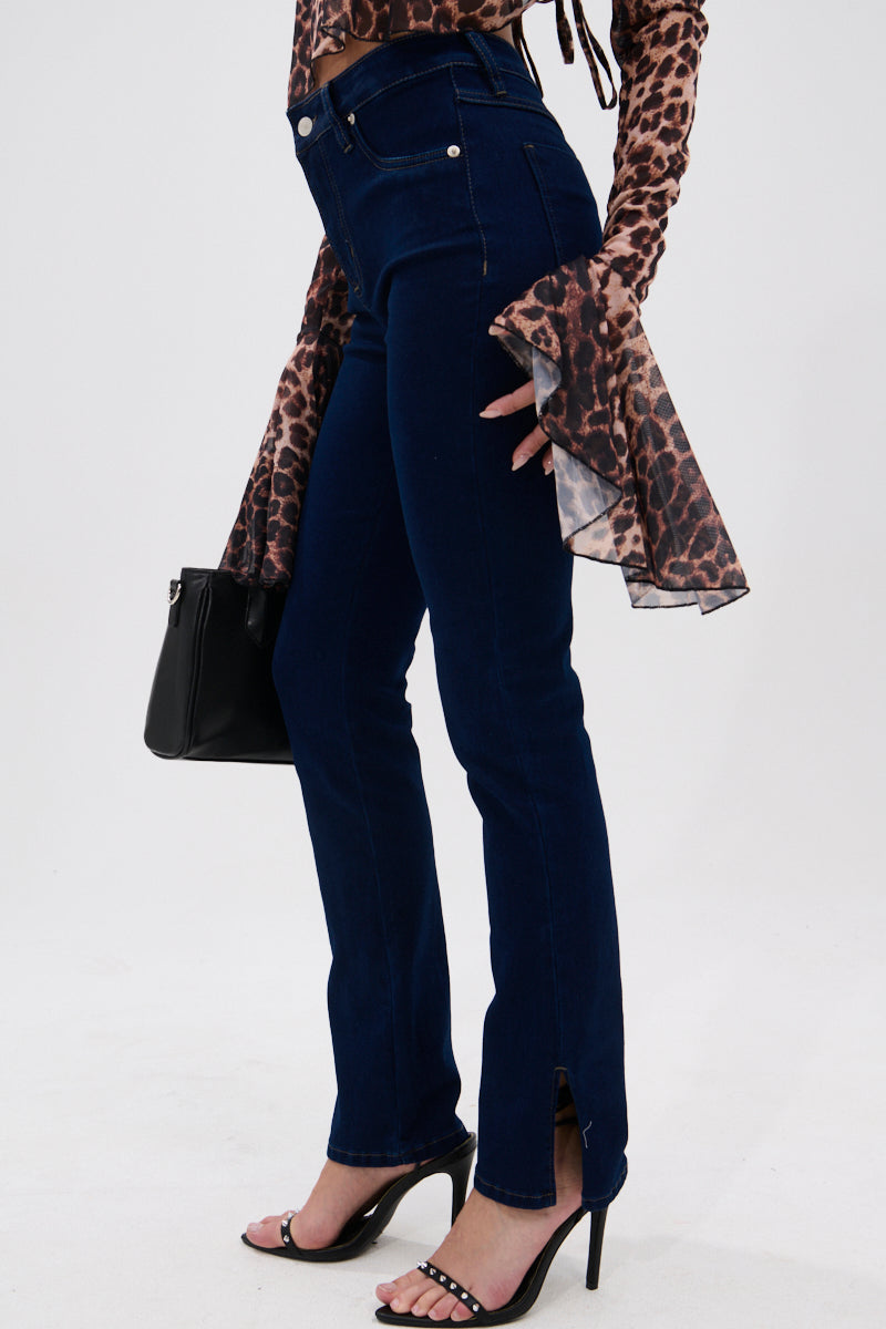 A person wearing THE BEST CORSET WAISTED FLARE DENIM jeans with front ankle slits, a brown leopard print long-sleeve top with flared cuffs, black heeled sandals, and carrying a small black bag.