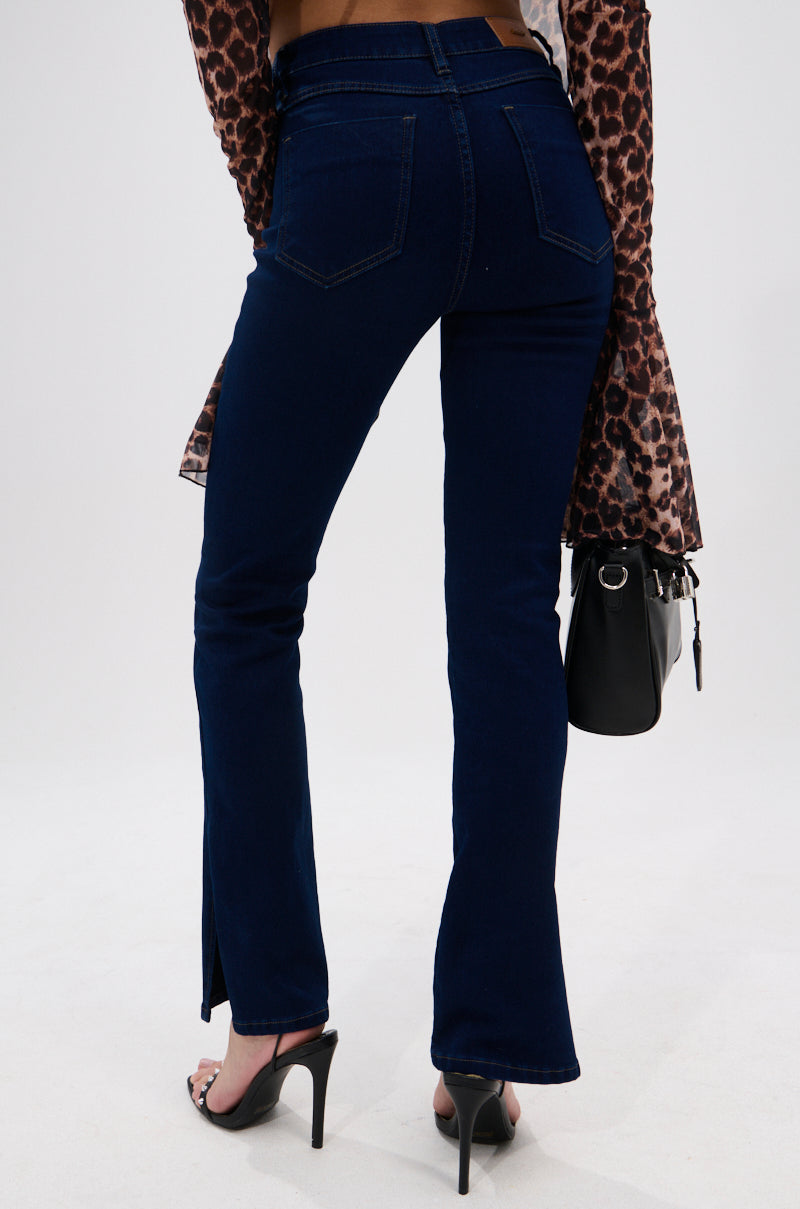 A person shown from the back wears THE BEST CORSET WAISTED FLARE DENIM in dark-wash stretch, paired with a brown and black leopard print bell-sleeve top, black high heels, and holds a black handbag.