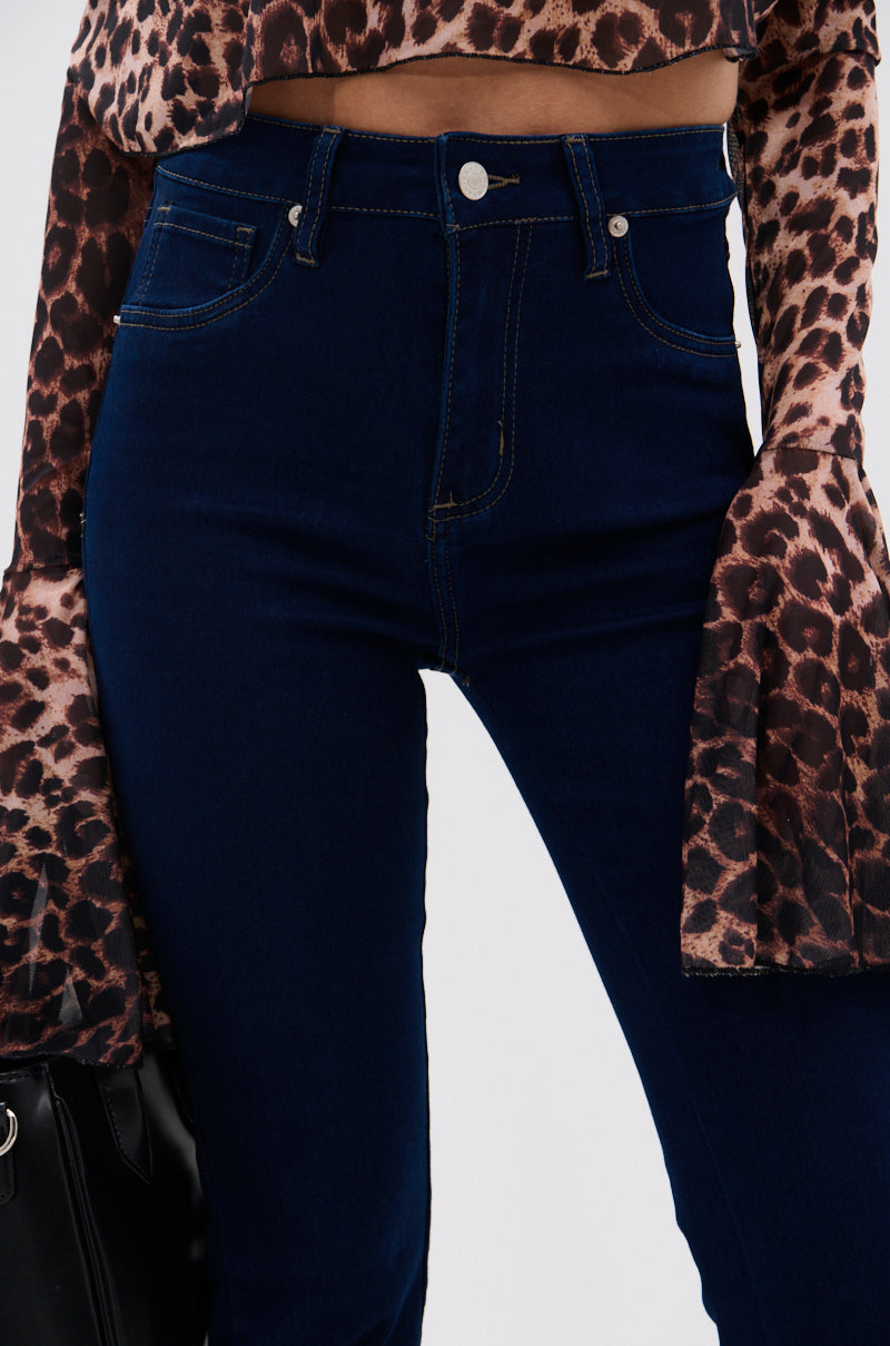 A person wearing THE BEST CORSET WAISTED FLARE DENIM, a long-sleeve leopard print top with flared cuffs, and holding a black bag.