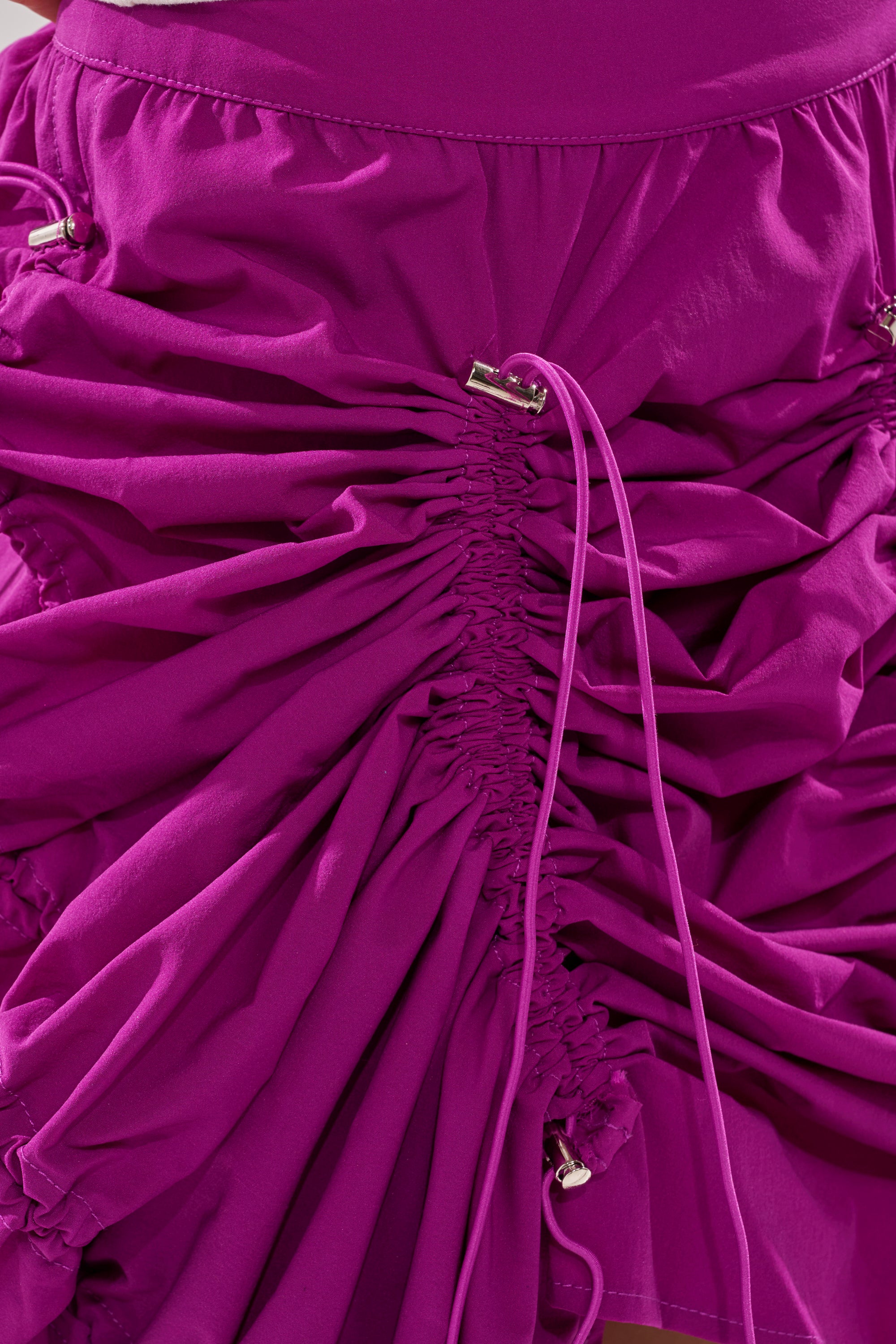 Close-up of the BELLA PARACHUTE MAXI SKIRT IN FUCHSIA, featuring vibrant color, gathered ruched details, and adjustable drawstrings for textured folds and a dynamic, layered look inspired by parachute-style design. 11