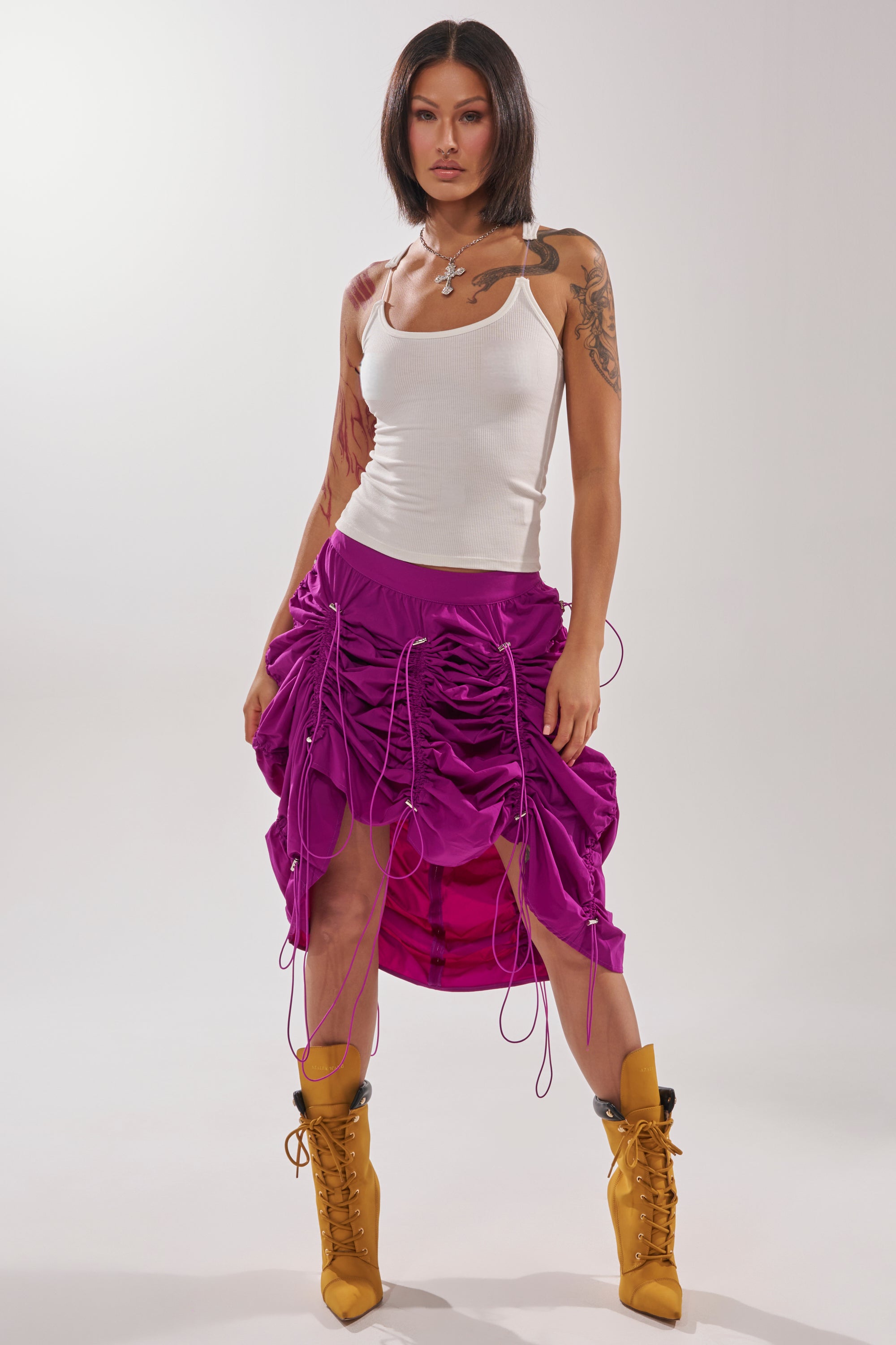 A woman poses confidently against a plain light background, wearing a white tank top, yellow lace-up boots, and the BELLA PARACHUTE MAXI SKIRT IN FUCHSIA. 8