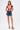 A woman in a colorful geometric tee, JULIE DENIM SKORT with chain belt, gold hoop earrings, and striped platform heels stands against a white background—a bold addition to any casual wardrobe.