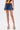 A person wearing a colorful sleeveless top, the JULIE DENIM SKORT in indigo wash, and high platform sandals with multicolored stripes stands against a plain white background—perfect for any casual wardrobe.