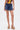 Someone wearing a vibrant sleeveless top, the JULIE DENIM SKORT in indigo wash with pleats, and high platform sandals with multicolored stripes stands against a white background—ideal for adding fun flair to your casual wardrobe.