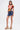 A woman models the JULIE DENIM SKORT in indigo wash with a chain belt, paired with a vibrant geometric top, large hoop earrings, and multicolored platform heels—an effortlessly chic look against a plain white background.
