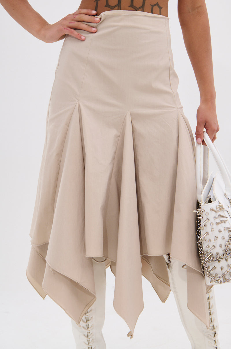 Wearing the HANNAH MIDI SKIRT with handkerchief pleats and a high waist, a person stands with one hand on their hip, holding a white bag with silver studs. White lace-up boots are visible beneath the skirt. 9