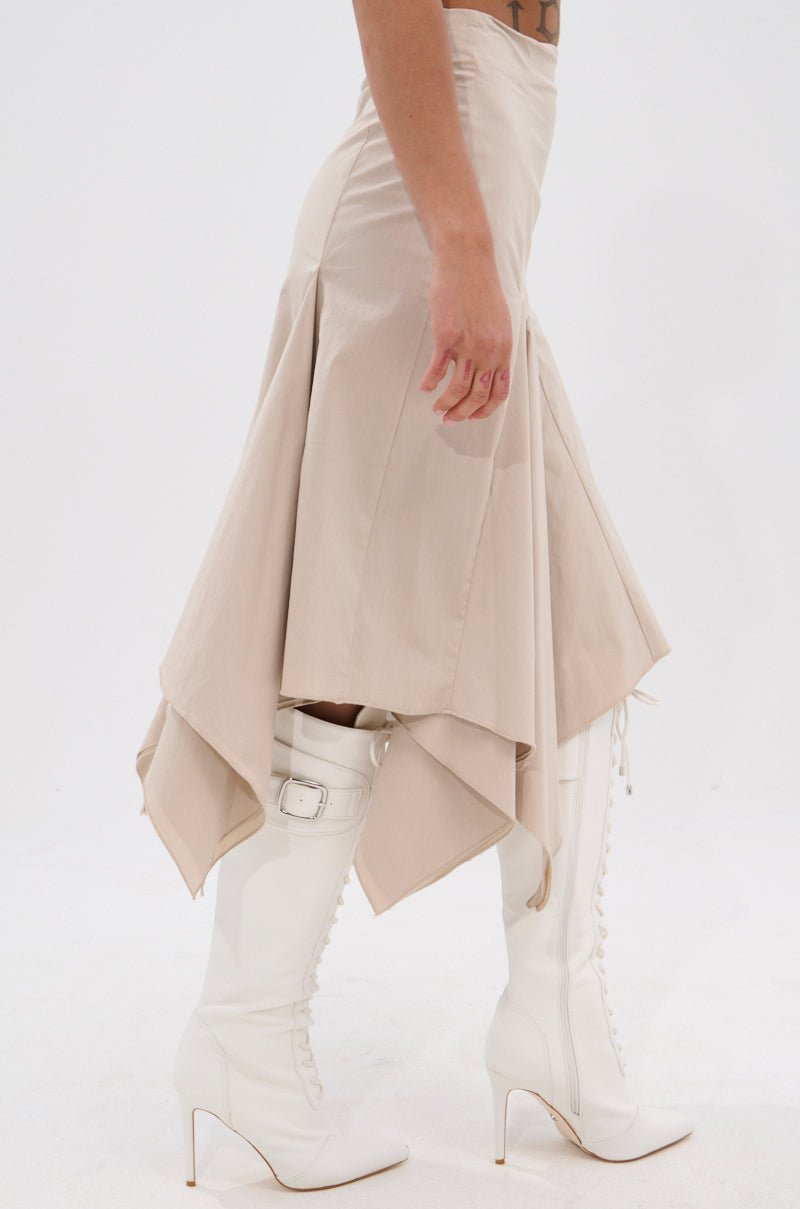 Wearing the HANNAH MIDI SKIRT with handkerchief pleats and white knee-high lace-up heeled boots, a person stands against a white background, showing only their lower body. 3