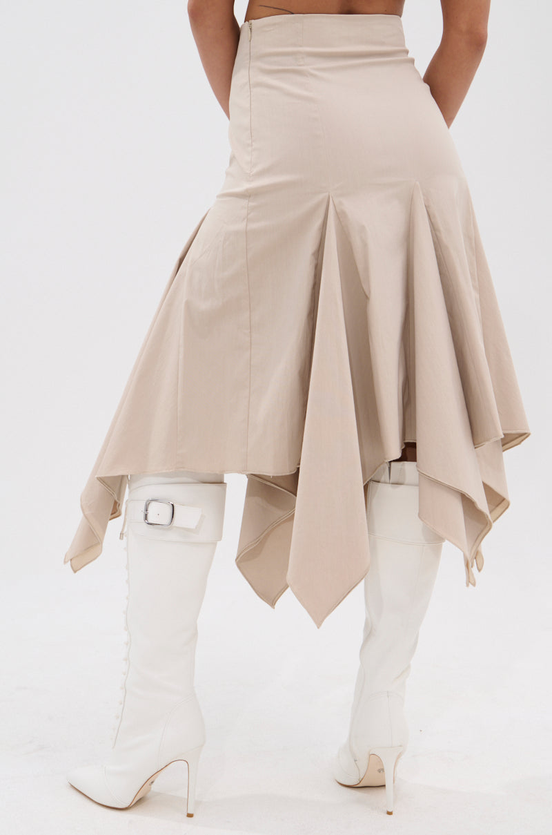 Someone is photographed from behind wearing the HANNAH MIDI SKIRT in beige, featuring high waist and asymmetrical handkerchief pleats, paired with white knee-high heeled boots with buckles, all set against a white background. 4