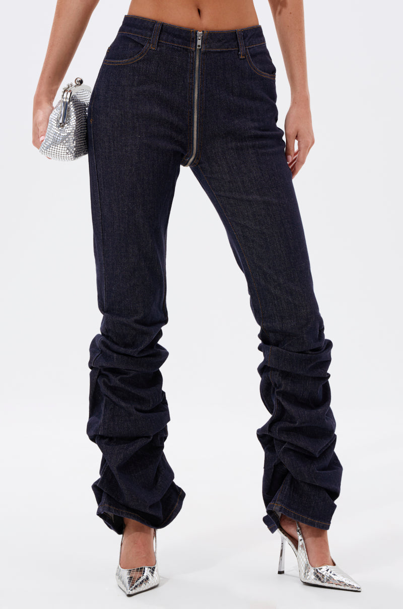 A person wearing the GET CRAZY RUCHED DENIM PANT in a high-rise, dark-wash style pairs it with a small silver handbag and pointed silver heels, shown from shoulders down against a plain white background. 0
