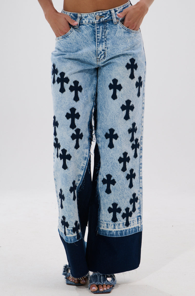 Person wearing CROSSED OUT WIDE LEG DENIM—high-waisted, vintage light-wash wide-leg jeans featuring black cross patterns and dark blue denim accents at the hem. Photo is cropped at waist and ankles.
