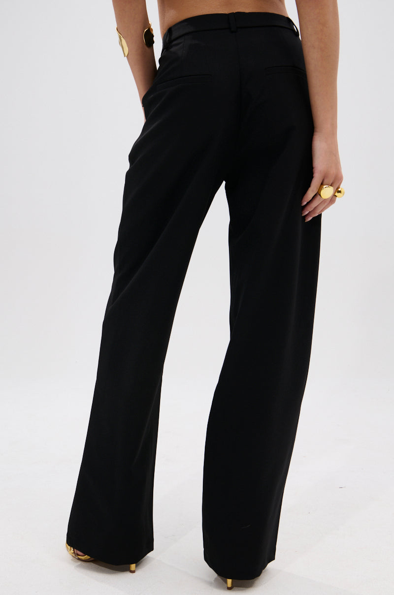 A person faces away, wearing the BUTTONED UP STRAIGHT LEG PANT with metallic gold buttons, along with gold rings and a bracelet, set against a plain white background. 4