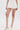 A person wearing the GUESS WHO MINI SKORT—a high-rise white skort with a faux leather belt—paired with a white top, white knee-high buckled gladiator sandals, and a small white handbag against a plain white background.