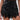 Someone is wearing the GOING OUT LACE TRIM LEATHER SHORTS, high-waisted faux leather shorts with lace trim at the hem and pocket flaps, styled with a sheer black lace top.