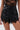 Someone is wearing the GOING OUT LACE TRIM LEATHER SHORTS, high-waisted faux leather shorts with lace trim at the hem and pocket flaps, styled with a sheer black lace top.