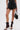 A woman models the GOING OUT LACE TRIM LEATHER SHORTS styled with a partial lace top, lace-up high heel boots, and a black handbag with a gold chain, all set against a plain white background.