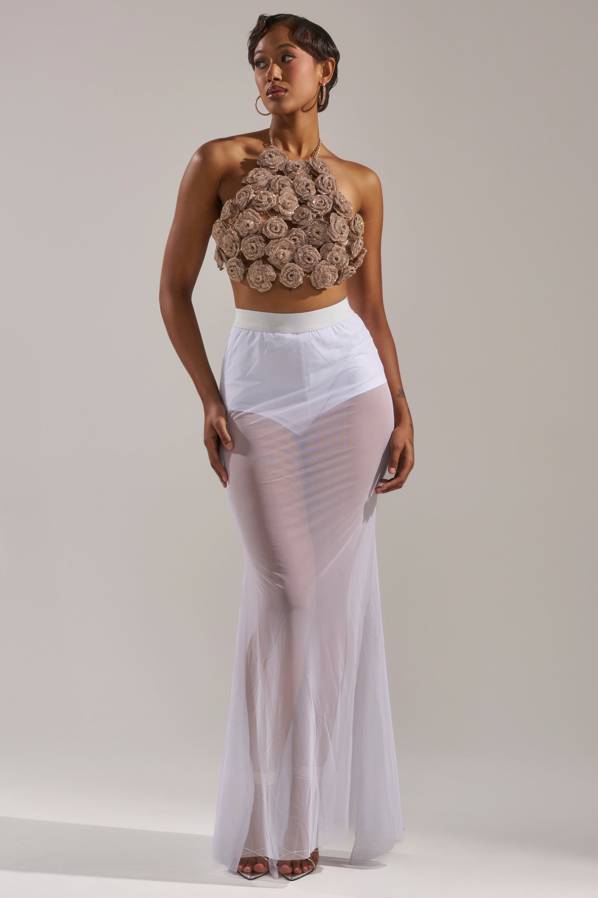 A woman poses in the DANCING QUEEN MESH MAXI SKIRT IN WHITE, styled with a sleeveless crop top and white undergarments—an effortlessly confident look ideal for layered evening ensembles. 0