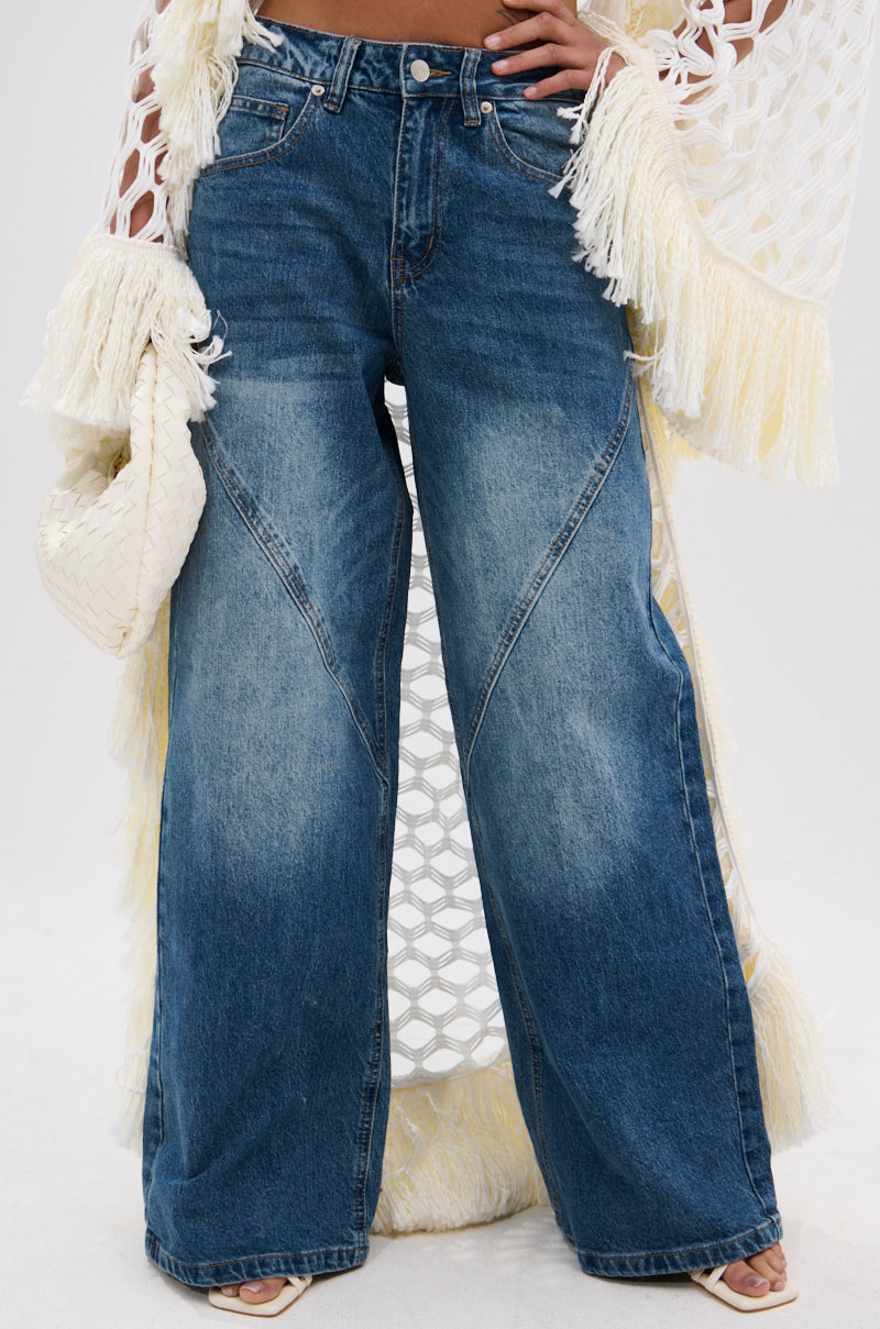 A person styles EXTREME RELAXED DENIM in a high-rise, ultra-wide-leg fit with faded details, paired with cream heeled sandals, a woven clutch, and a cream and yellow fringed crochet cover-up.