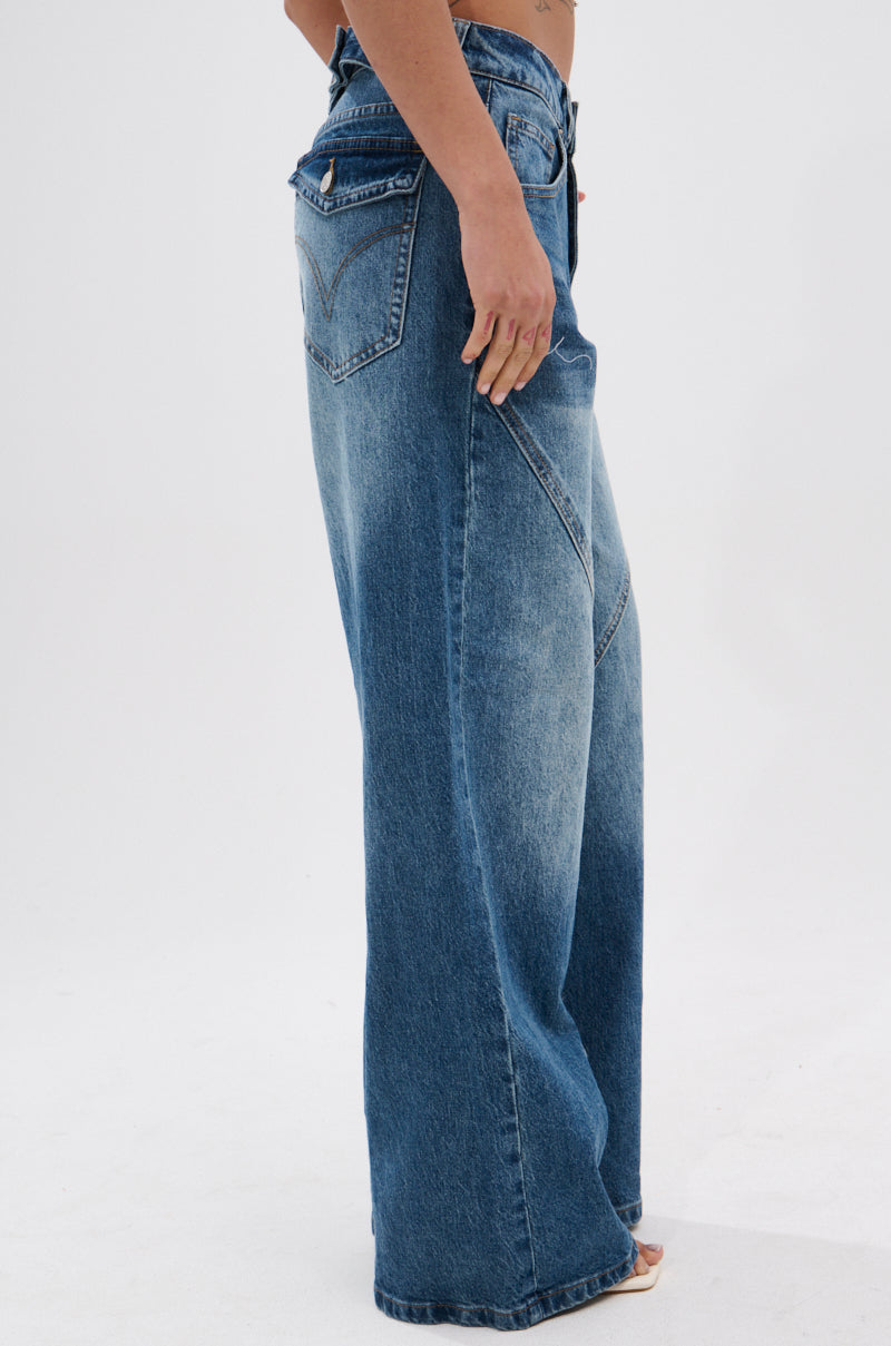 A person models the EXTREME RELAXED DENIM high-waisted, ultra-wide leg blue jeans with a faded wash, visible pockets, and seam details, standing sideways against a plain white background.