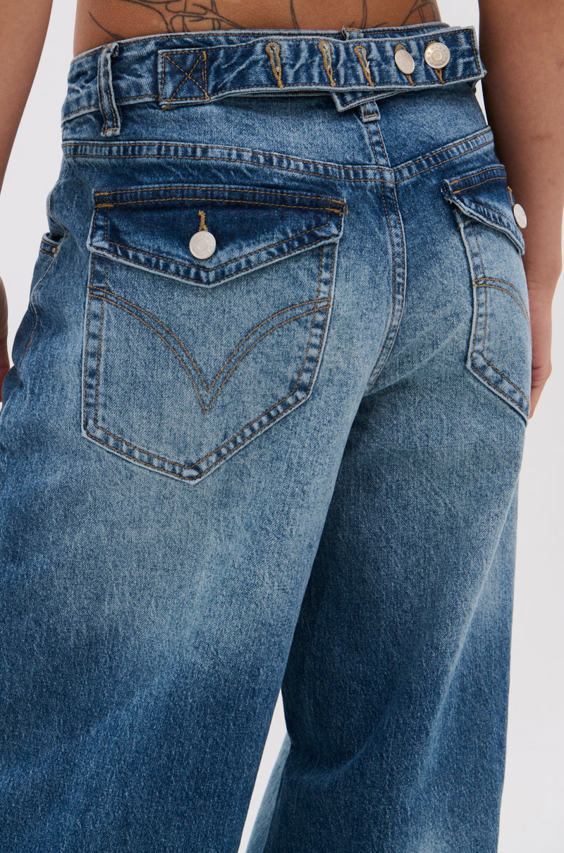 Close-up of the back of a person wearing EXTREME RELAXED DENIM, featuring an ultra-wide leg, high-rise fit, contrast stitching, metallic buttons, visible belt loops, and a tattoo on their lower back.