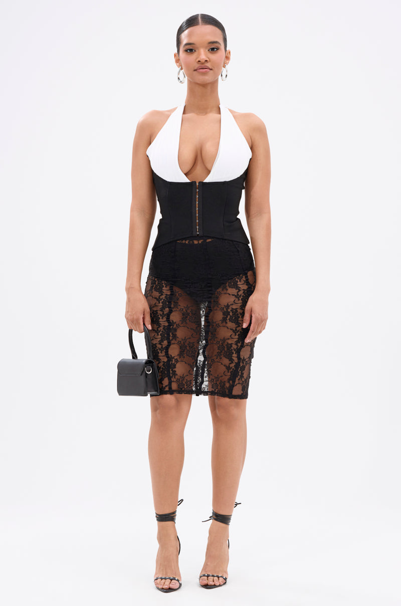 A woman wears the BABY PLEASE PLEASE LACE MIDI SKIRT, styled with a white halter top, black corset, black strappy heels, and a small black handbag. Her hair is pulled back and she maintains a neutral expression. 7